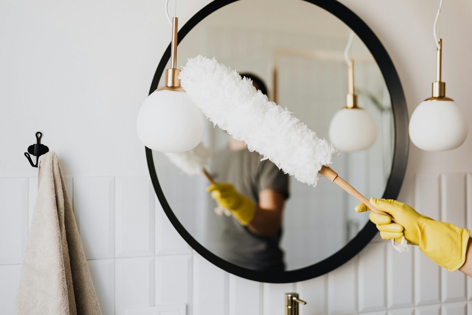 Une personne nettoyant un élégant miroir de salle de bain avec un plumeau moelleux et des gants jaunes.